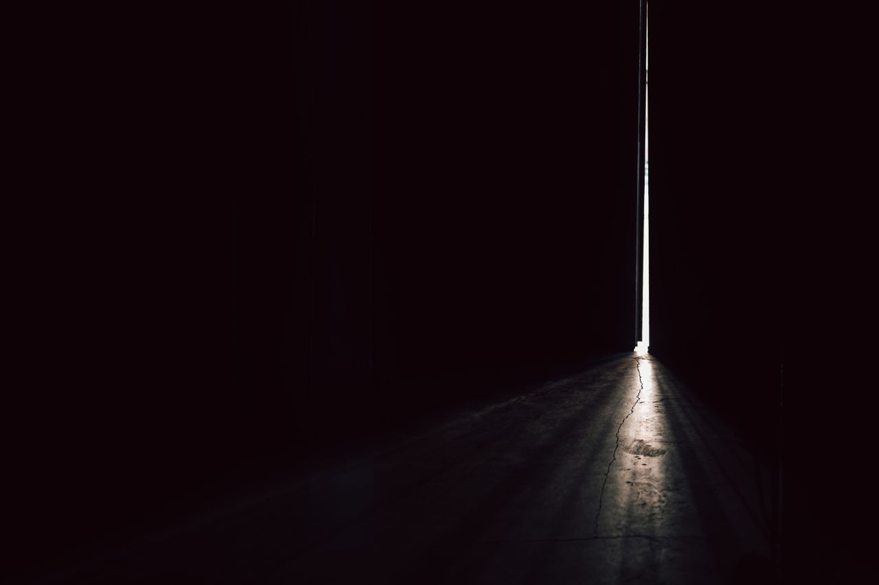 A narrow beam of light piercing through a dark room from a slightly open door.