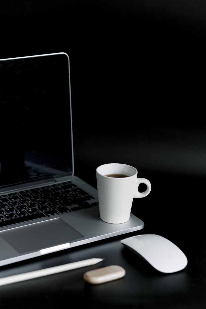 A sleek minimalist setup featuring a laptop, coffee cup, and gadgets on a black background.